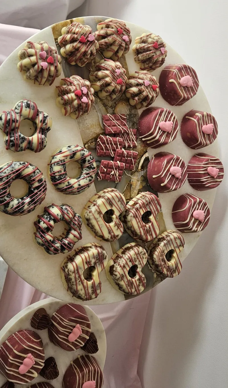 Schaal met chocolade donuts in Oreo-stijl, mini-repen en roze traktaties met babyvoetjes