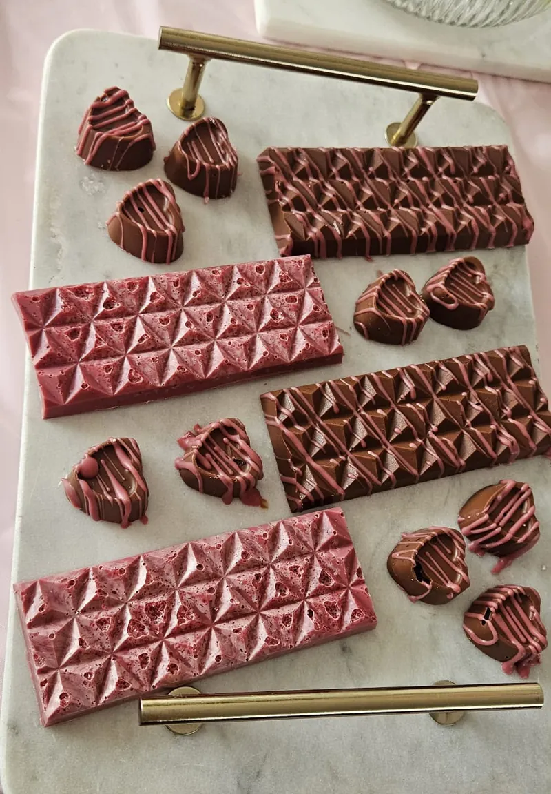 Dikke chocoladerepen met geometrisch reliëf en hartvormige bonbons op een marmeren dienblad